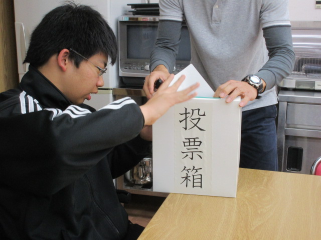 代筆で記入された投票用紙を投票箱に入れる男子盲生