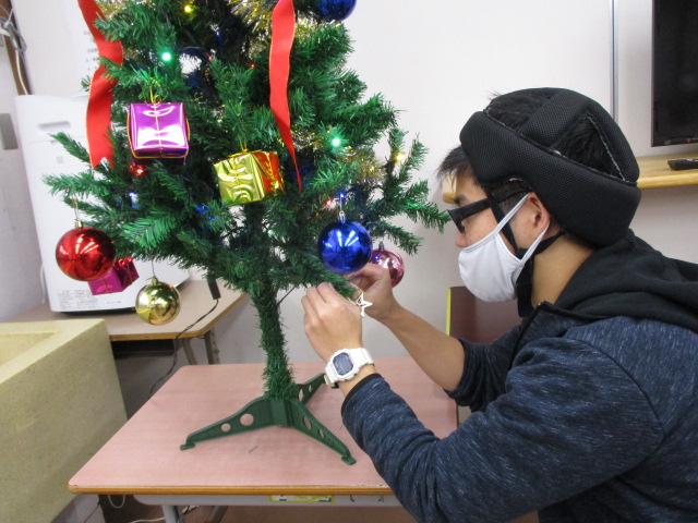 男子舎生がクリスマスツリーに飾りをつけている写真