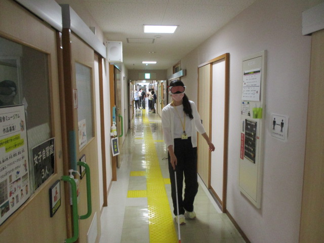 アイマスクを着け白杖で廊下を歩く職員