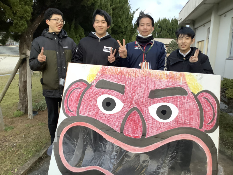 鬼の顔の後ろで並んで写る舎生
