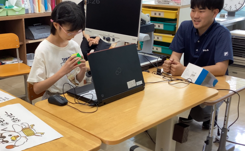 ルービックキューブを揃えて画面越しに披露する本校児童